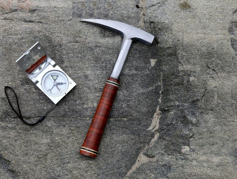 Geologist's hammer and compass on a rock outcrop